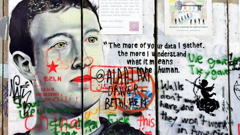The image features a mural of a man with a serious expression, surrounded by various graffiti texts and symbols on a wall. The artwork appears to critique technology and data privacy, with phrases expressing strong opinions on personal data and surveillance.