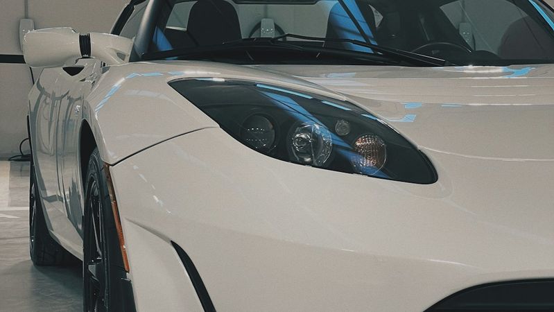 A close-up view of a sleek white sports car parked indoors. The car features a streamlined design with distinctive headlights and black accents, showcasing its modern engineering.