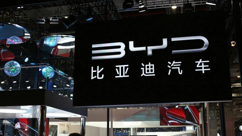 The image showcases a prominent display booth from BYD, a Chinese automotive manufacturer, at an auto show. The booth features a large illuminated sign with the BYD logo and Chinese characters, drawing attention from attendees.