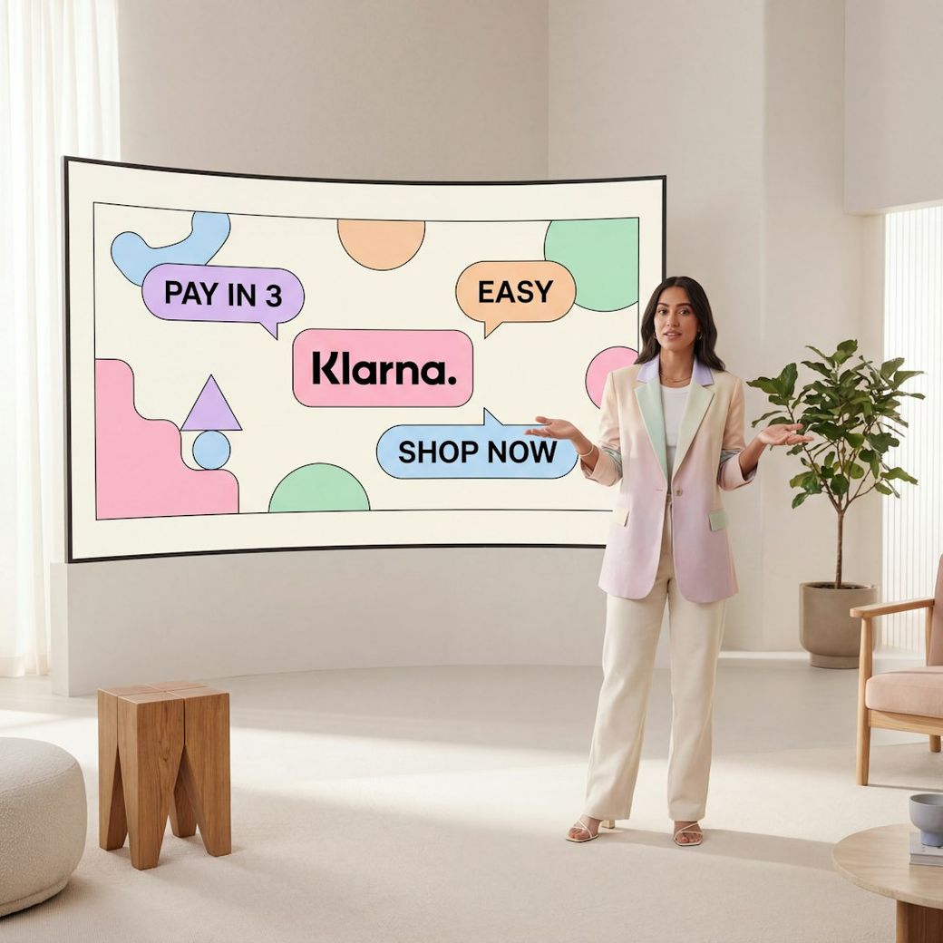 A woman stands in a modern interior space, gesturing towards a large screen displaying colorful shapes and promotional text. The screen features the Klarna logo alongside phrases such as 'PAY IN 3' and 'EASY', indicating a shopping or payment service. — Credit: Photo by Eric Human on Unsplash