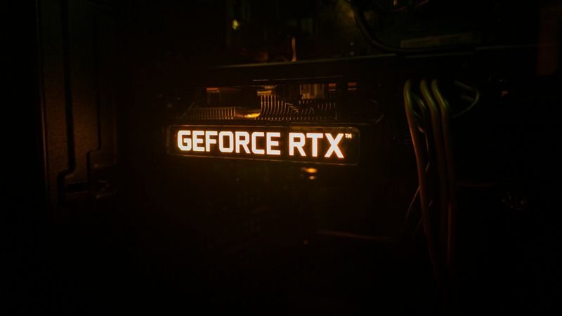The image features a close-up view of a computer graphics card, specifically highlighting the illuminated 'GEFORCE RTX' branding. The lighting emphasizes the technology and cooling components within the system.