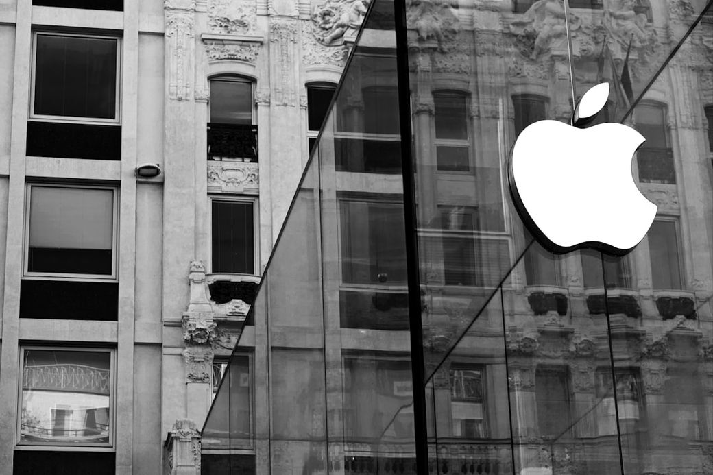 The image features the exterior of an Apple store, showcasing a prominent Apple logo on a glass facade. The background displays architectural details of a historic building, contrasting with the modern design of the store. — Credit: Photo by Niccolò Chiamori on Unsplash