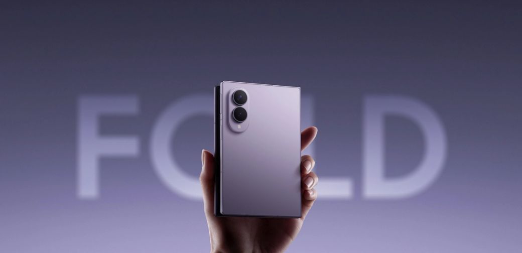 The image showcases a hand holding a sleek, modern folding smartphone with a reflective purple finish. In the background, the word 'FOLD' is prominently displayed, emphasizing the device's folding feature, which aligns with the latest advancements in mobile technology by Samsung.