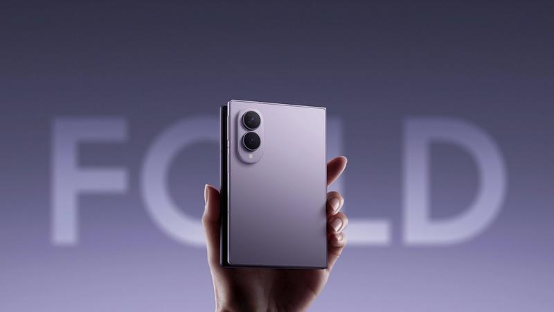 The image showcases a hand holding a sleek, modern folding smartphone with a reflective purple finish. In the background, the word 'FOLD' is prominently displayed, emphasizing the device's folding feature, which aligns with the latest advancements in mobile technology by Samsung.