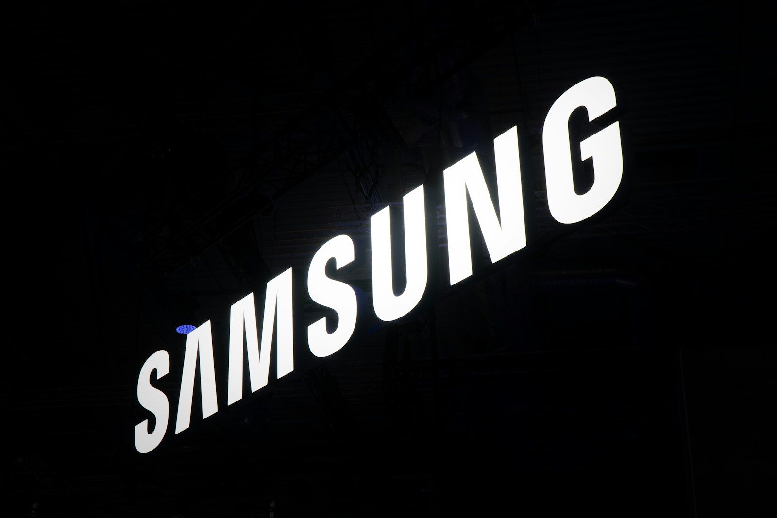 The image features the illuminated logo of Samsung, prominently displayed against a dark background. The logo is captured in a way that emphasizes its modern and sleek design.