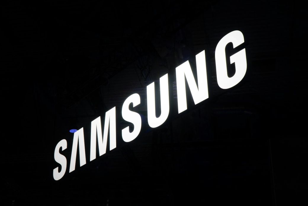 The image features the illuminated logo of Samsung, prominently displayed against a dark background. The logo is captured in a way that emphasizes its modern and sleek design. — Credit: Photo by Jonathan Kemper / Unsplash