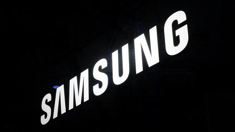 The image features the illuminated logo of Samsung, prominently displayed against a dark background. The logo is captured in a way that emphasizes its modern and sleek design.