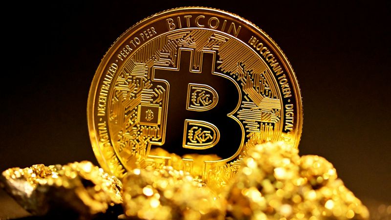 An image depicting a prominent Bitcoin cryptocurrency coin placed atop a cluster of gold nuggets. The vibrant gold and detailed design of the Bitcoin coin stands out against the dark background, symbolizing the intersection of digital and physical assets.