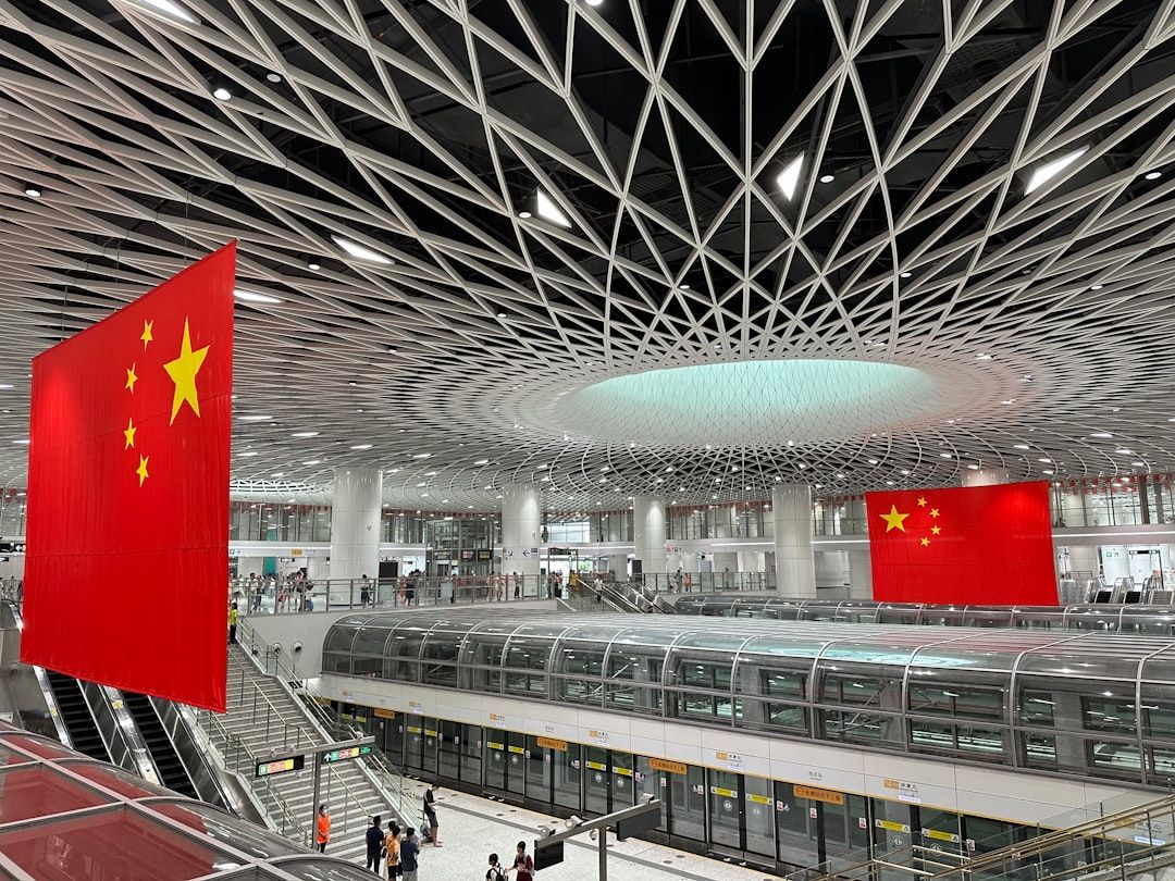 The image shows the interior of a modern transportation hub characterized by its intricate architectural design. Large Chinese flags are prominently displayed, emphasizing the national identity within the space.