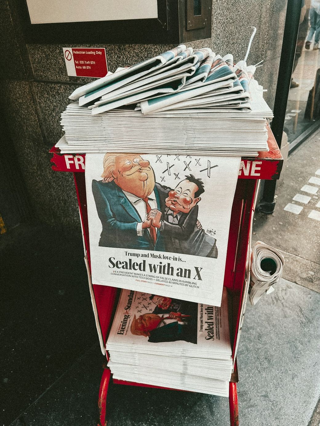 A newspaper stand features a prominent cartoon cover illustrating a satirical take on a meeting between Donald Trump and Kim Jong-un. The headline reads 'Sealed With an X' with a caricature capturing the two figures in a humorous light. — Credit: Photo by Samuel Regan-Asante on Unsplash