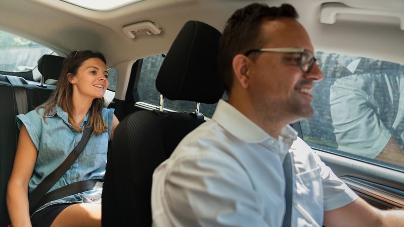 A man driving a car with a woman sitting in the passenger seat. The woman appears to be enjoying the ride, while the man is focused on driving.