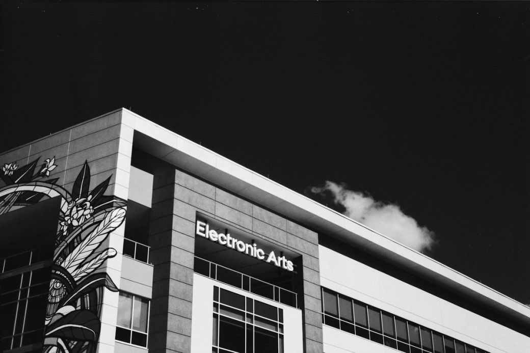 The image features the exterior of the Electronic Arts building, showcasing a modern architectural design with a stylized mural on the side. Clear skies with a single cloud can be seen above. — Credit: Photo by Sergei Novikov / Unsplash
