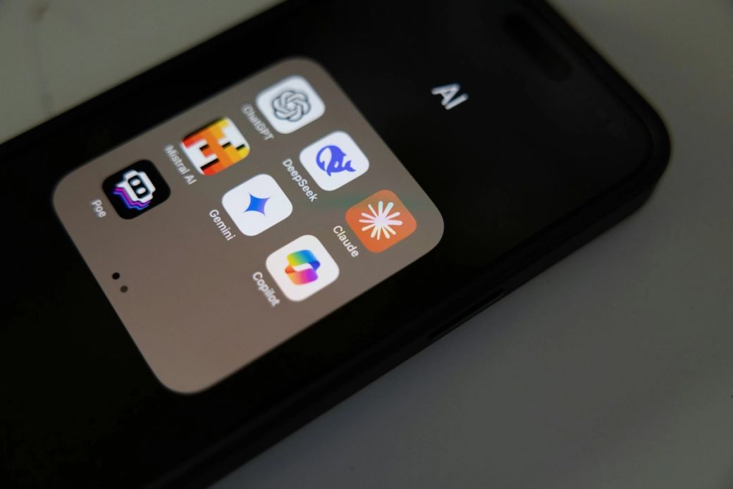 The image shows a close-up of a smartphone screen displaying various AI-related applications. The apps include ChatGPT, Deepl, Gemini, Claude, and Copilot, all housed within an 'AI' folder. — Credit: Photo by Solen Feyissa / Unsplash