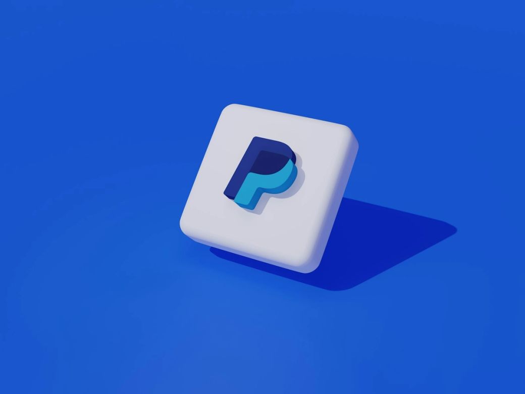 A stylized representation of the PayPal logo on a blue background, showcasing a modern and digital aesthetic. The logo appears in a three-dimensional format, emphasizing the brand's identity in the financial technology sector. — Credit: Photo by Muhammad Asyfaul / Unsplash