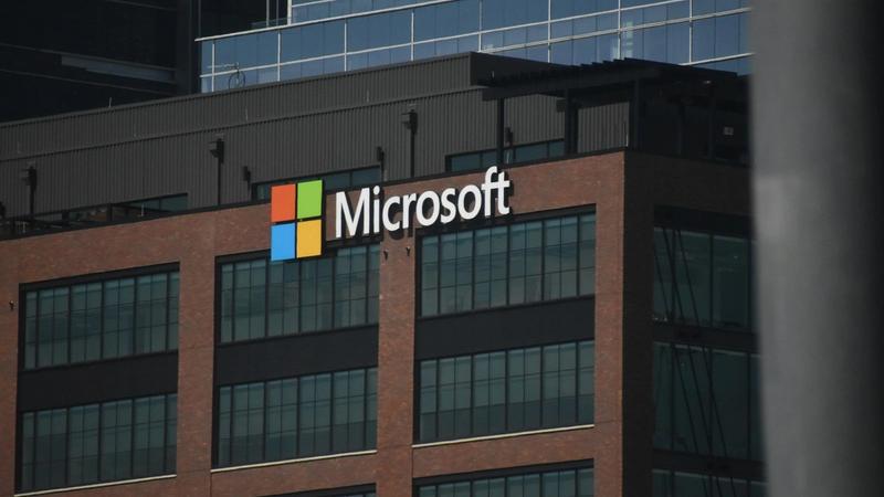 The image features the exterior of a commercial building prominently displaying the Microsoft logo. The structure is modern with large windows and a distinctive facade.