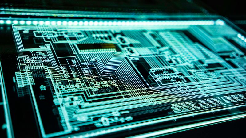 The image depicts a close-up view of a circuit board with intricate electronic pathways and components illuminated in a glowing blue light. This visually striking representation highlights the complexity and design of modern electronics.