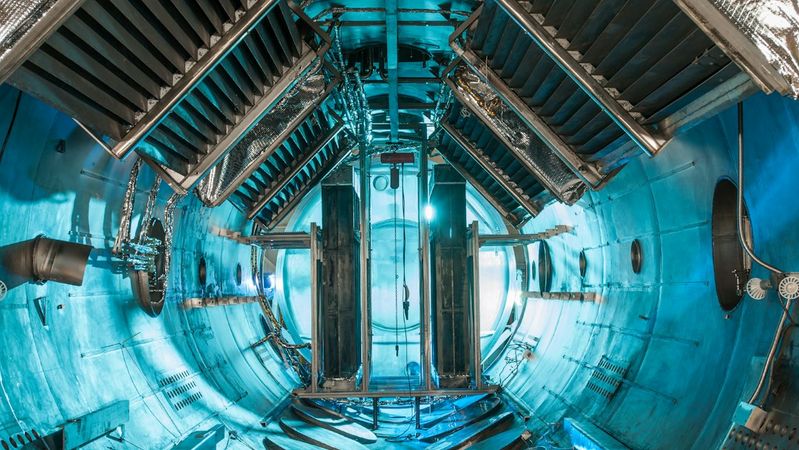 The image depicts the interior of a testing chamber with a futuristic design, showcasing a series of metallic surfaces and equipment surrounded by a blue-lit environment. The space appears engineered for scientific or experimental purposes.