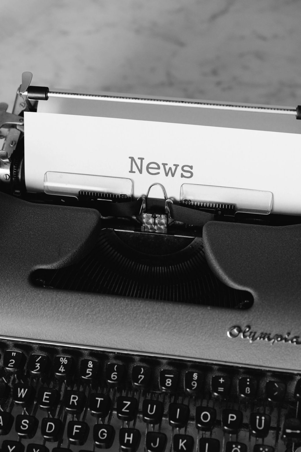 A close-up view of a typewriter with a piece of paper inserted, displaying the word 'News'. The typewriter's keys and mechanics are visible, emphasizing the vintage writing tool. — Credit: Photo by Markus Winkler / Unsplash