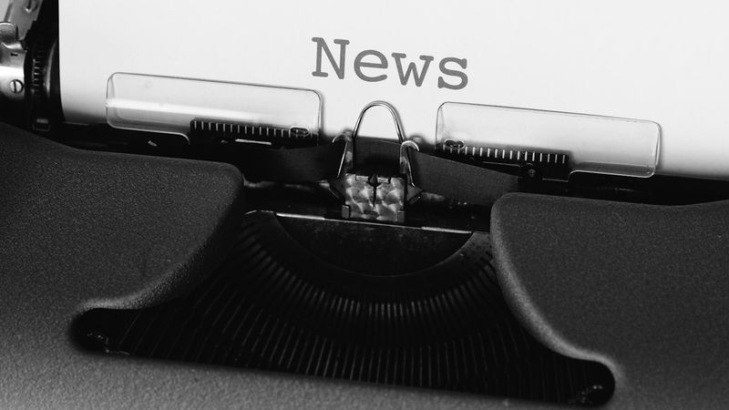 A close-up view of a typewriter with a piece of paper inserted, displaying the word 'News'. The typewriter's keys and mechanics are visible, emphasizing the vintage writing tool.