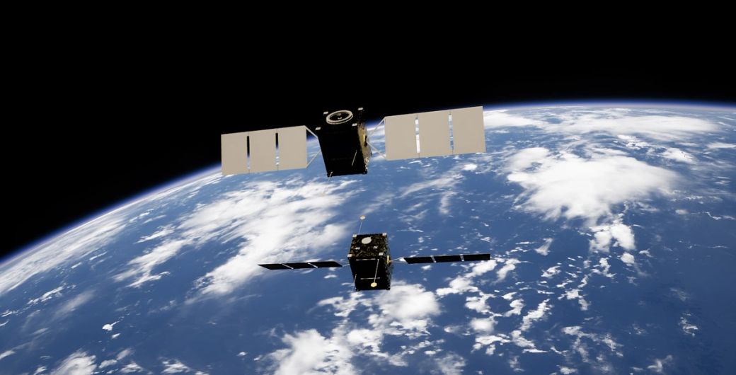 The image depicts two satellites in low Earth orbit, set against the backdrop of the planet's surface and cloud cover. The satellite structures are visible, showcasing their solar panels and technology. — Credit: Photo by Kevin Stadnyk / Unsplash