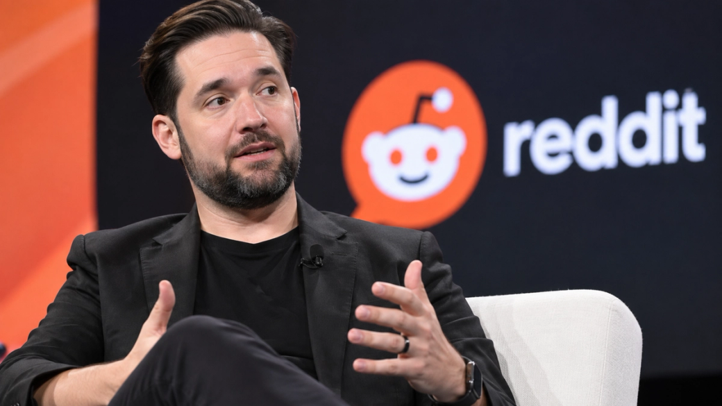 The image features Alexis Ohanian, co-founder of Reddit, engaged in a discussion. He appears seated on a couch, with his hands gesturing as he speaks, set against a backdrop displaying the Reddit logo.