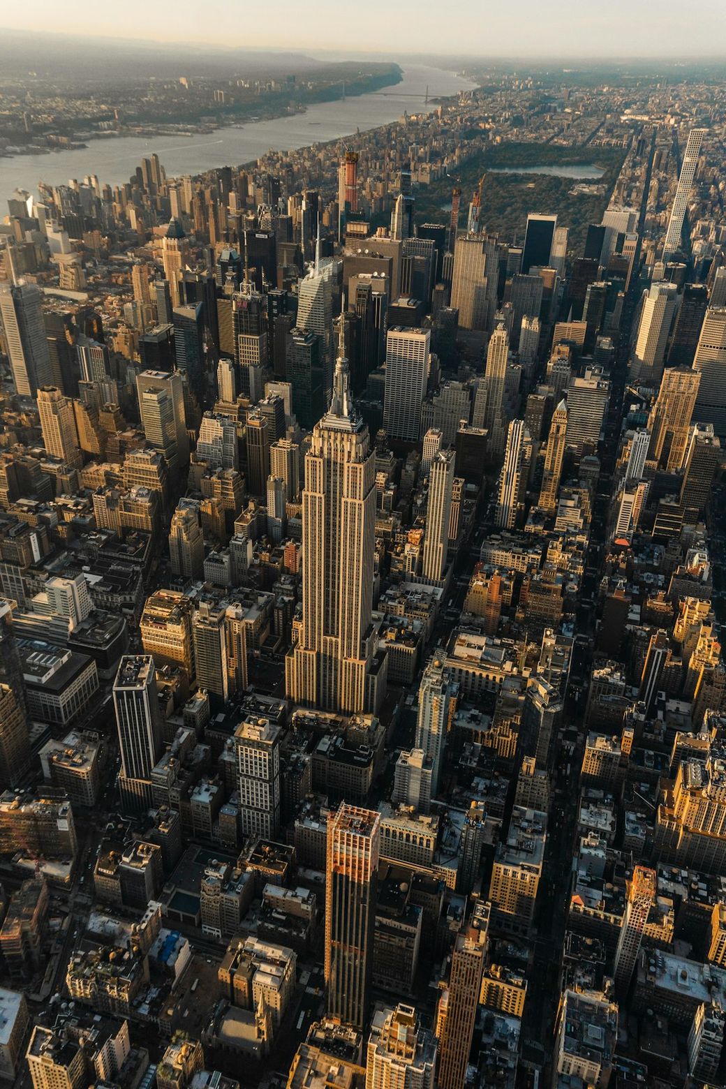 Aerial view of New York City with a focus on the iconic Empire State Building. The image captures the dense urban landscape, showcasing skyscrapers and the outline of the Hudson River in the background during sunset. — Credit: Photo by Triston Dunn on Unsplash