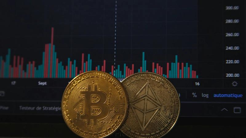 The image features two cryptocurrency coins, Bitcoin and Ethereum, placed in front of a digital financial chart displaying price fluctuations. The background shows a trading interface with colorful bar graphs, suggesting a focus on cryptocurrency markets.