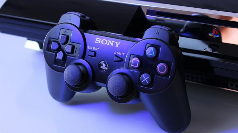 The image showcases a close-up view of a Sony PlayStation controller placed next to a PlayStation console. The lighting gives a modern and sleek appearance to the gaming setup.