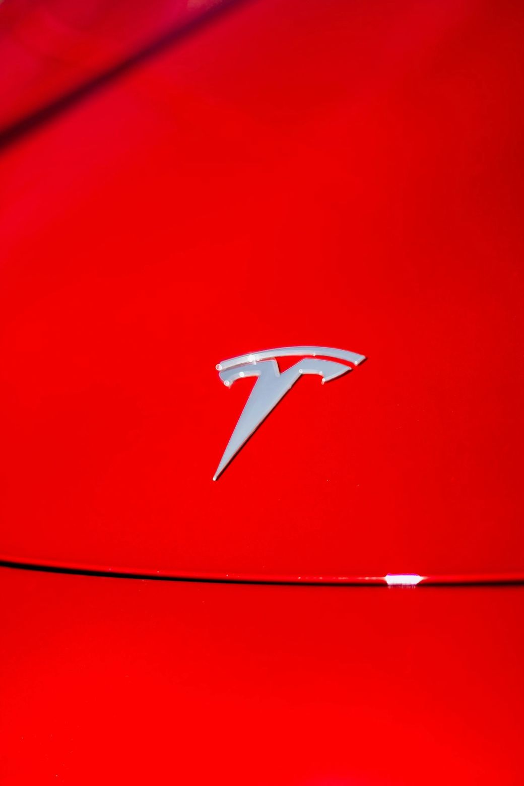 The image features the Tesla logo prominently displayed against a bright red background. The logo, known for its sleek and modern design, symbolizes the electric vehicle company's innovative approach to automotive technology. — Credit: Photo by Willian Cittadin / Unsplash