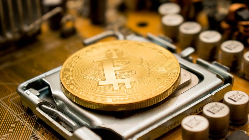 The image showcases a close-up of a golden Bitcoin coin resting on a computer circuit board. The intricate details of the electronic components surrounding the cryptocurrency highlight its technological foundation.