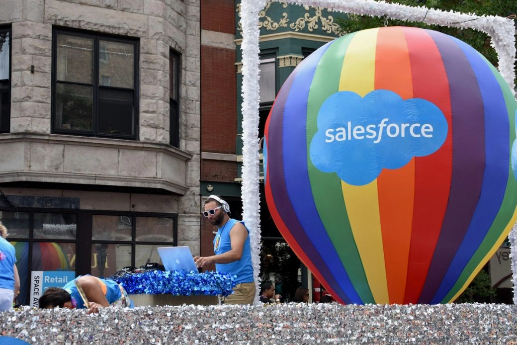 The image captures a vibrant parade scene featuring a DJ performing on a float, accompanied by a large colorful hot air balloon displaying the Salesforce logo. The atmosphere is festive and lively, indicative of a community celebration or event. — Credit: Photo by Jonathan Smith / Unsplash
