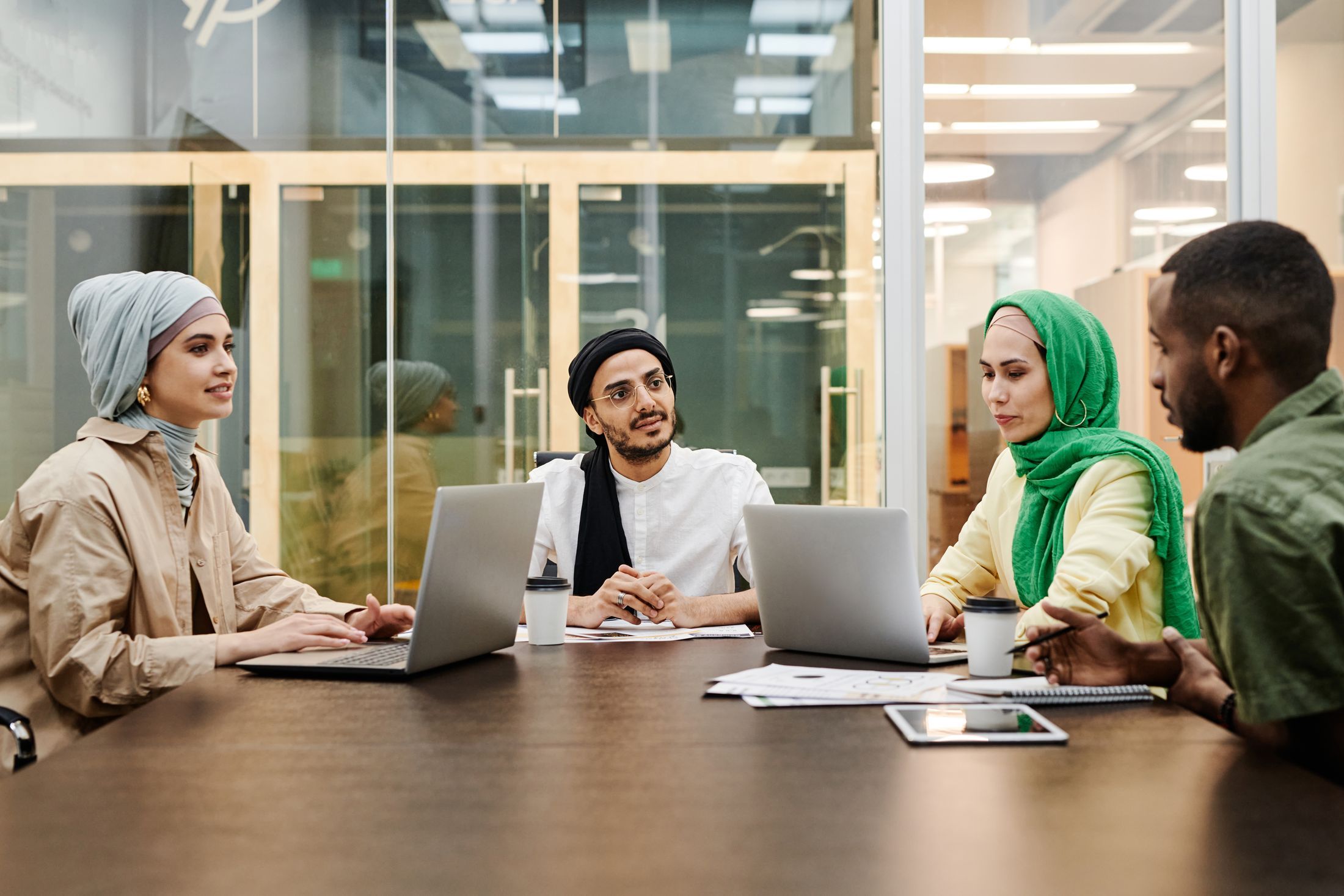 Colleagues exchanging ideas around laptops in a modern meeting space
