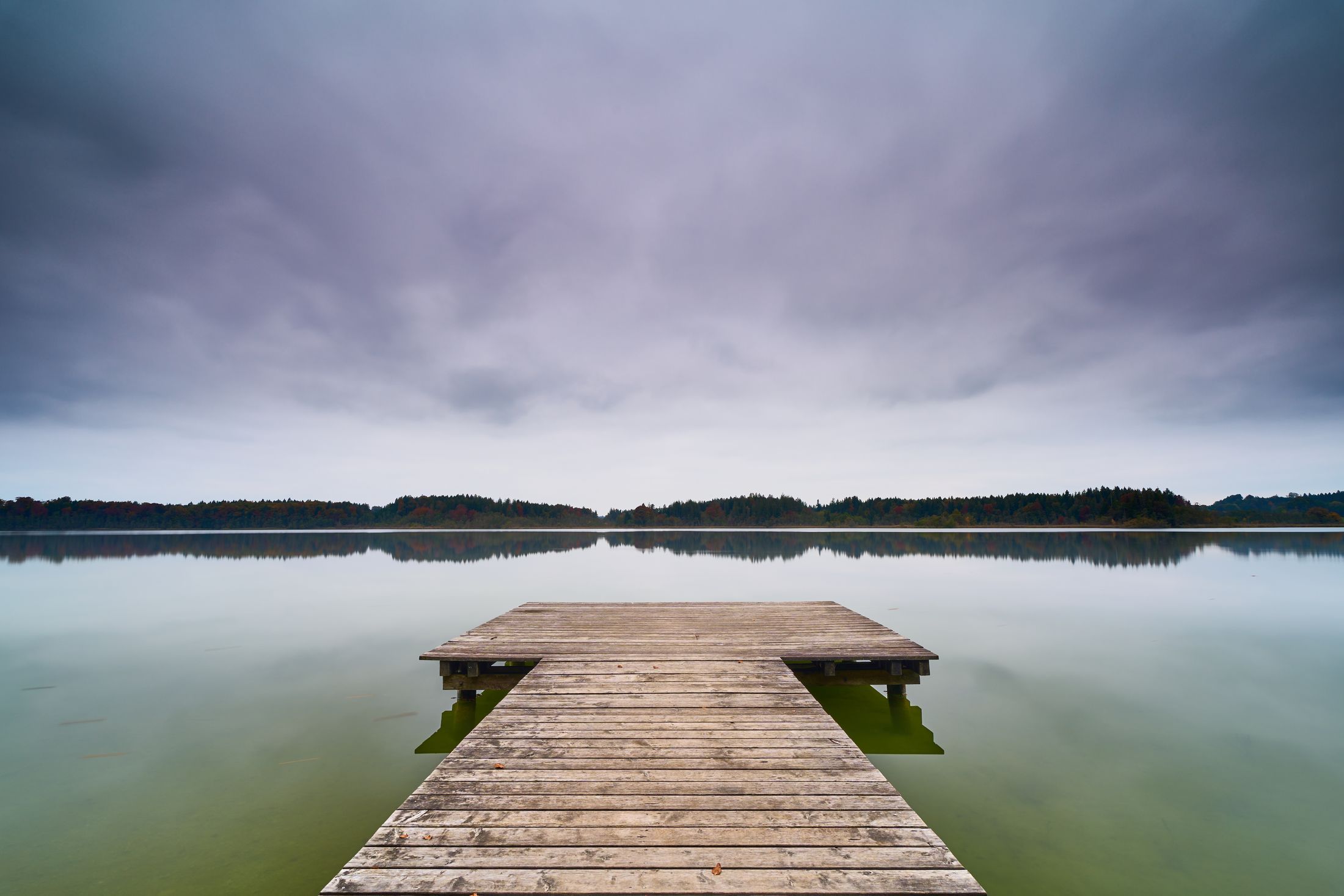 Expansive view of a wooden dock extending over a calm lake under a cloudy sky, capturing tranquility and nature.
