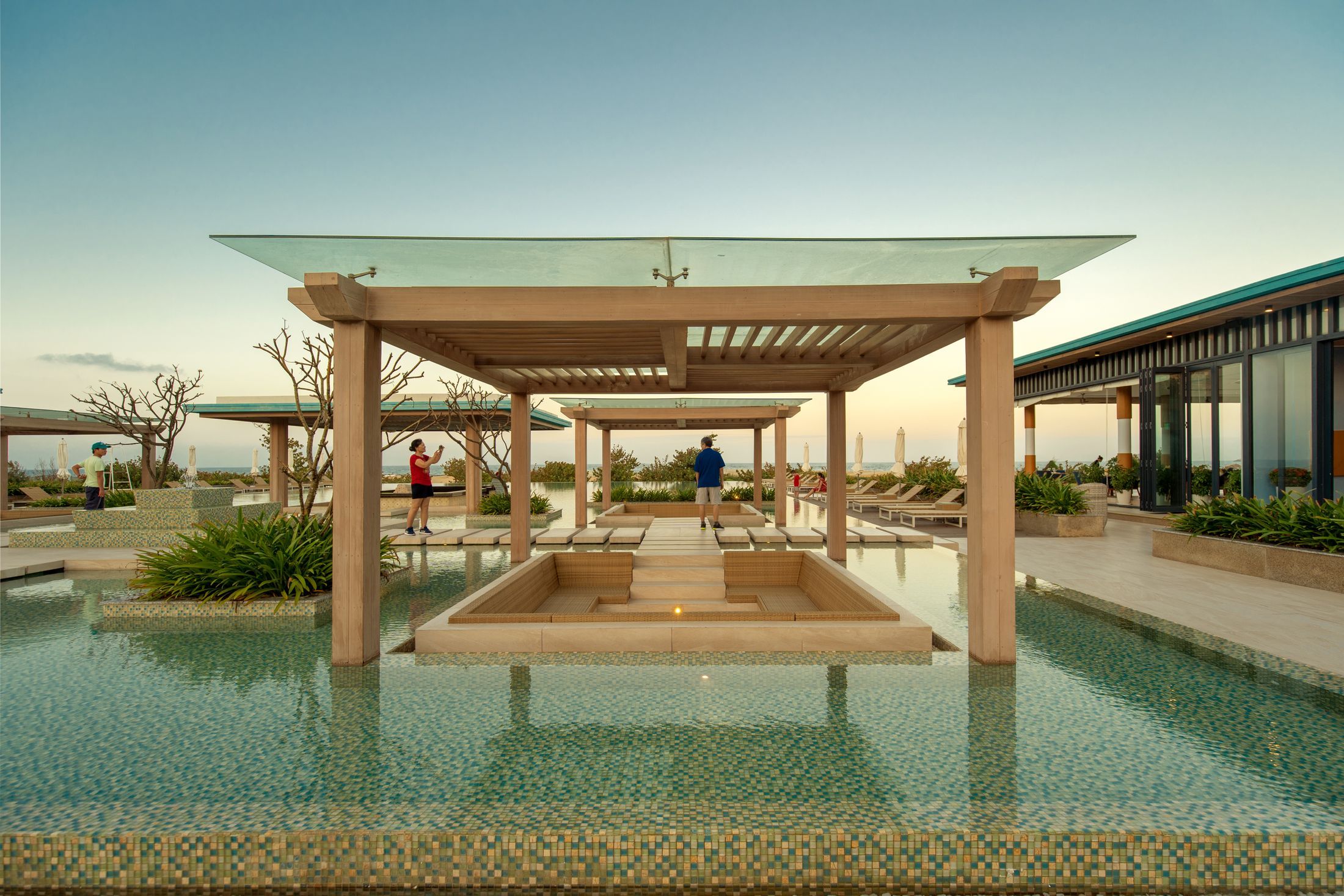 Elegant resort pool area with tourists and modern design at sunset in Vietnam.