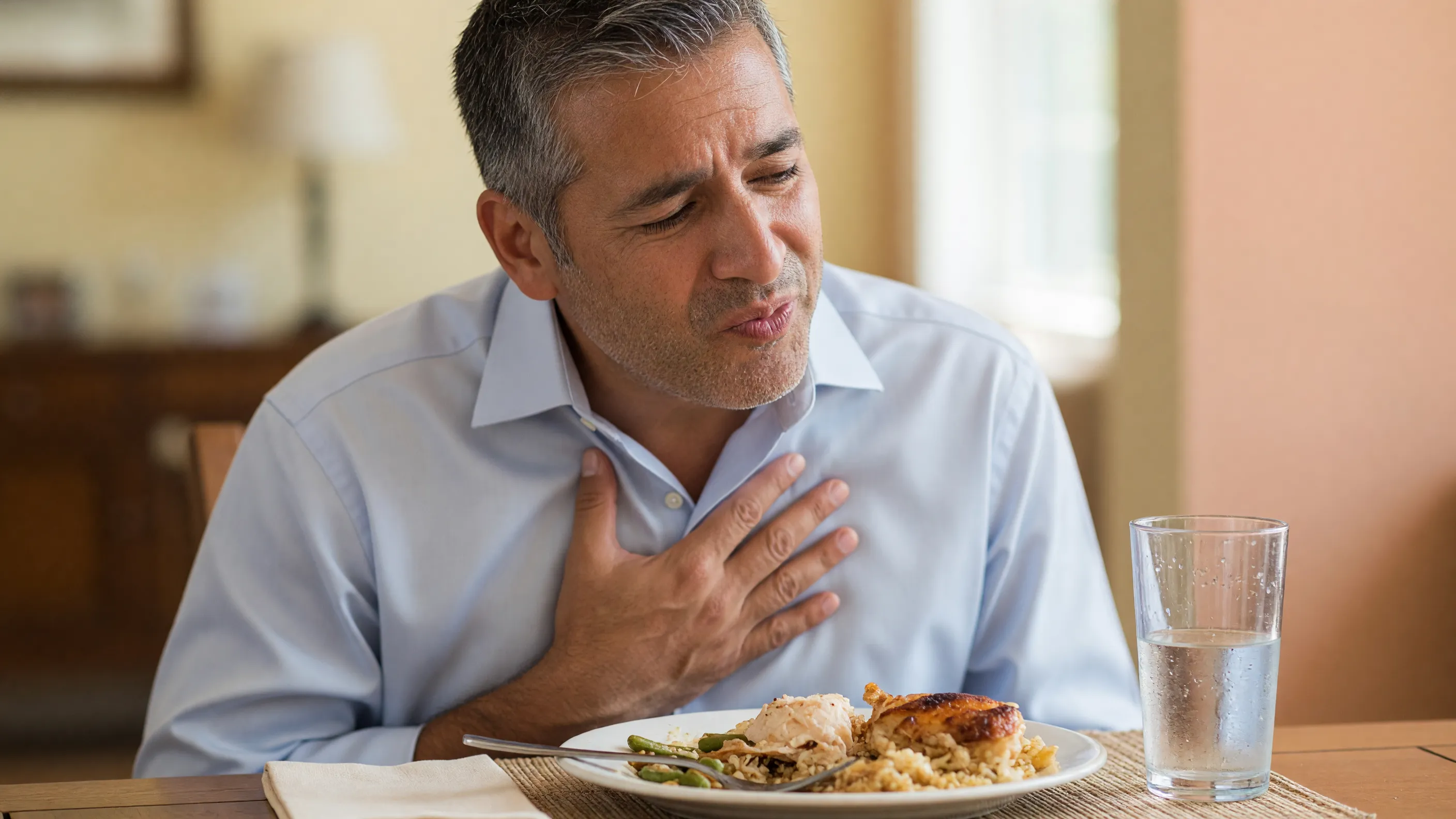 Man experiencing difficulty swallowing, a key achalasia symptom, holding his chest at the dinner table