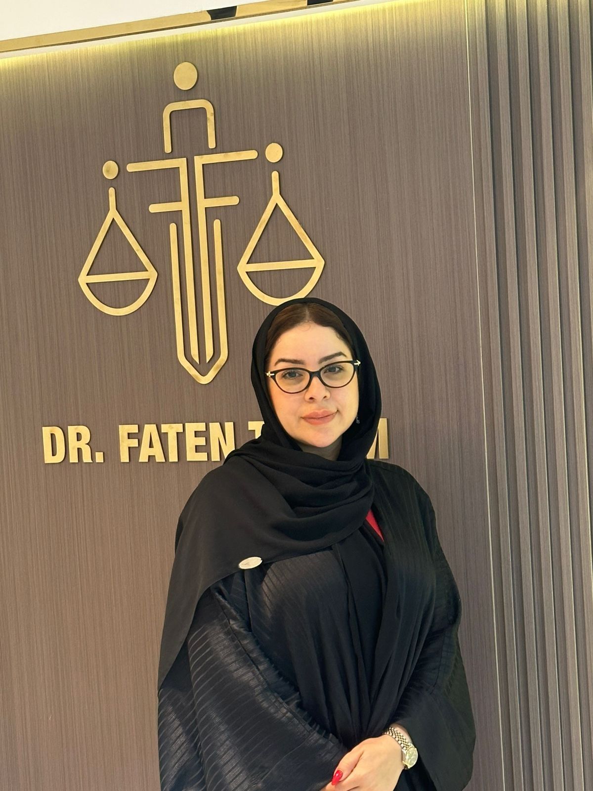 Dr. Faten Tamim standing beside the firm’s gold emblem