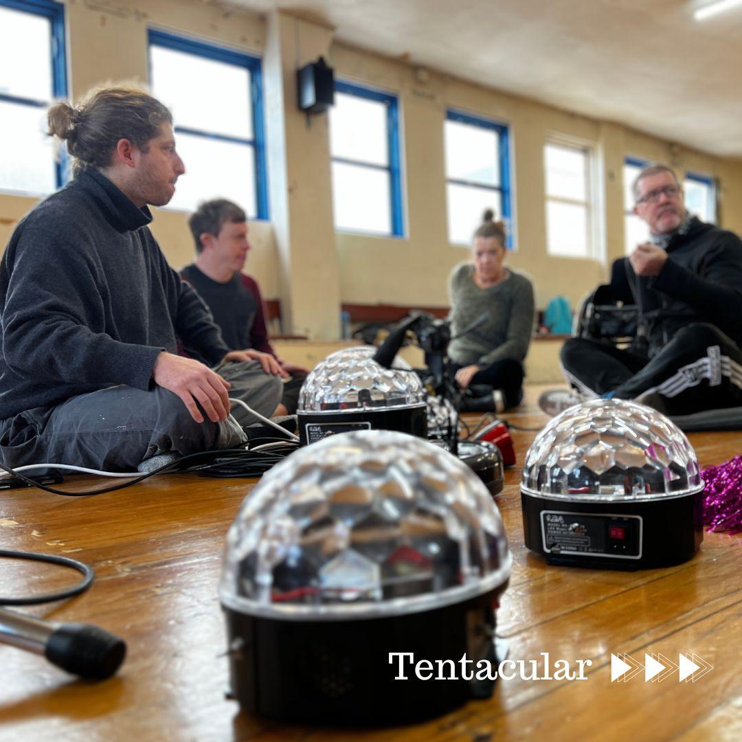 Three strobe lights on the ground in a worn wooden floored dance hall; they are sonic transducers for the work Tentacular. Around them sit four people in discussion about their use. The room is not warm, as reflected in the long-sleeved layers of the dancers in discussion.