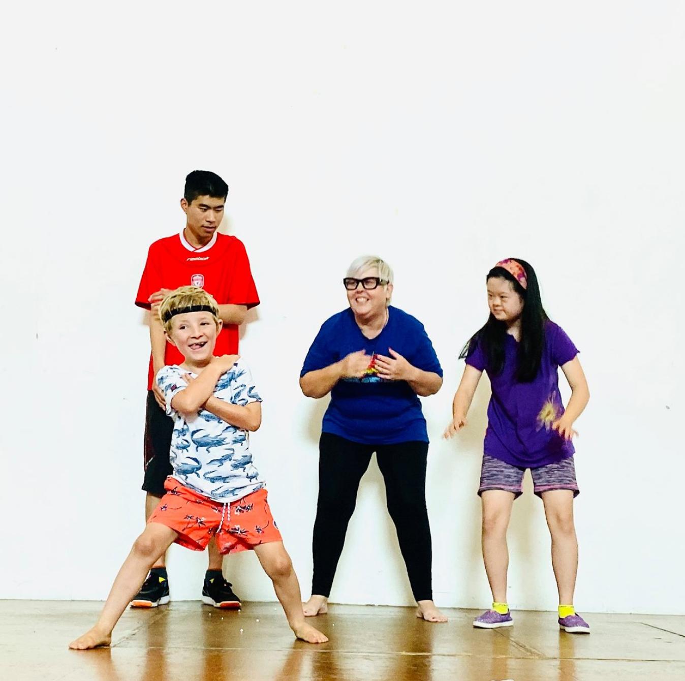 Four dancers of diverse ages and ethnicities are standing in various dance poses, having fun and smiling.