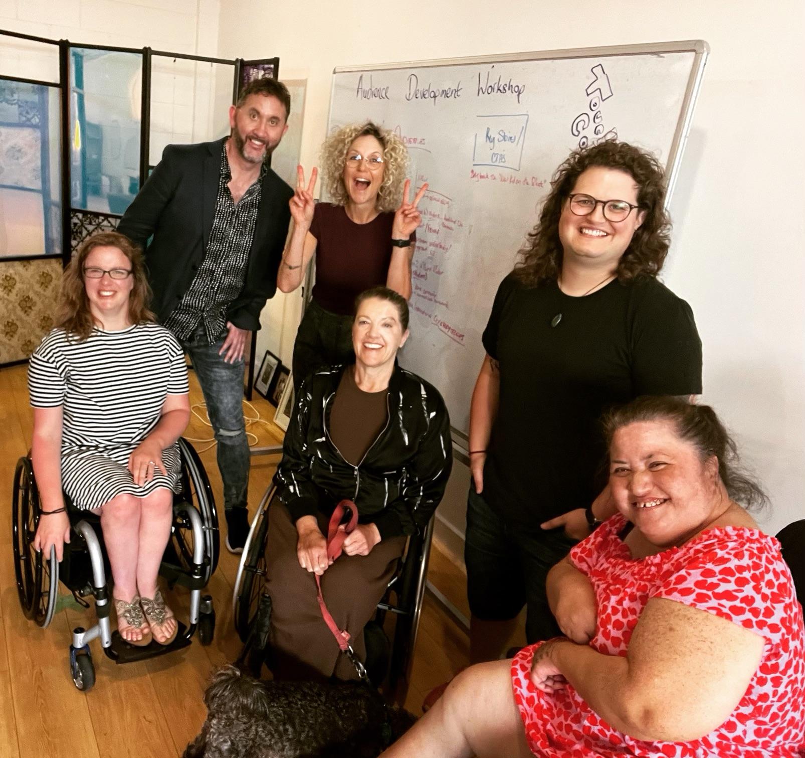 Six people in front of a whiteboard - Three standing behind three people sitting in wheelchairs.