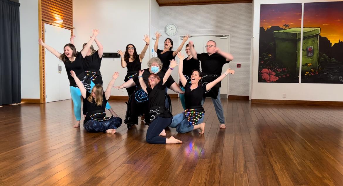 Touch Compass Saturday Class year-end performance, with people standing and kneeling on the ground, wearing black tops, their arms up in the air, with huge grins.