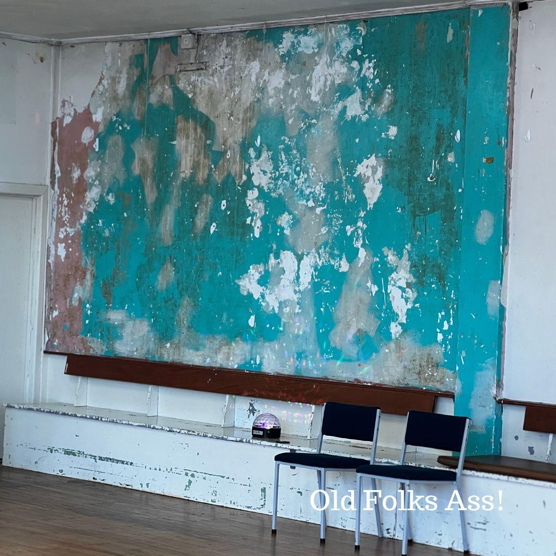 A beaten, peeling, old wall, turquoise, clay and white colours mottled in at once a weathered and beautiful wall. The basic office chairs on the floor in front of the wall, with a strobe light on the old 1930s built-in storage benches.