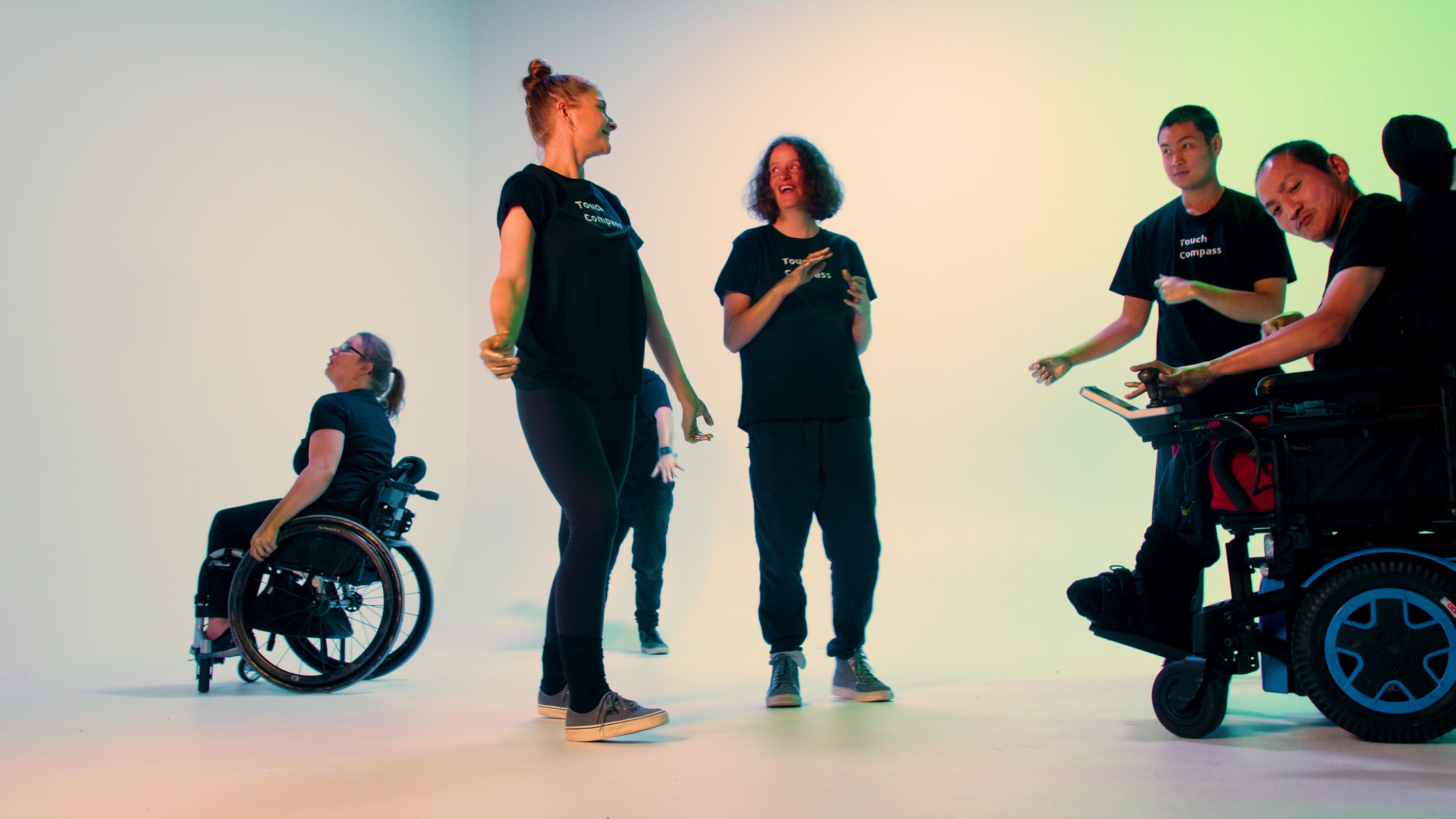 Six people dressed in black outfits dancing as part of a Matariki project, two in wheelchairs, four standing.