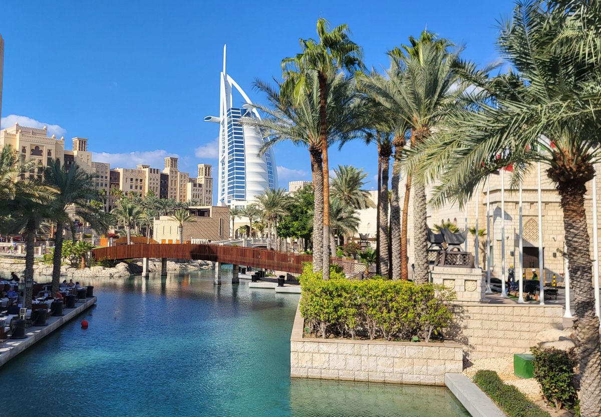Un canal bordé de palmiers au Souk Madinat Jumeirah, avec une passerelle en bois et le Burj Al Arab au fond
