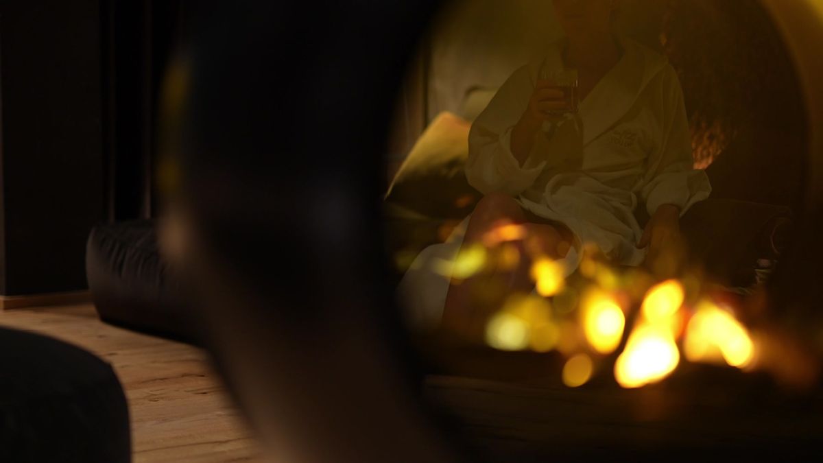 A person in a white bathrobe holding a drink by the fire at Mount Med Resort