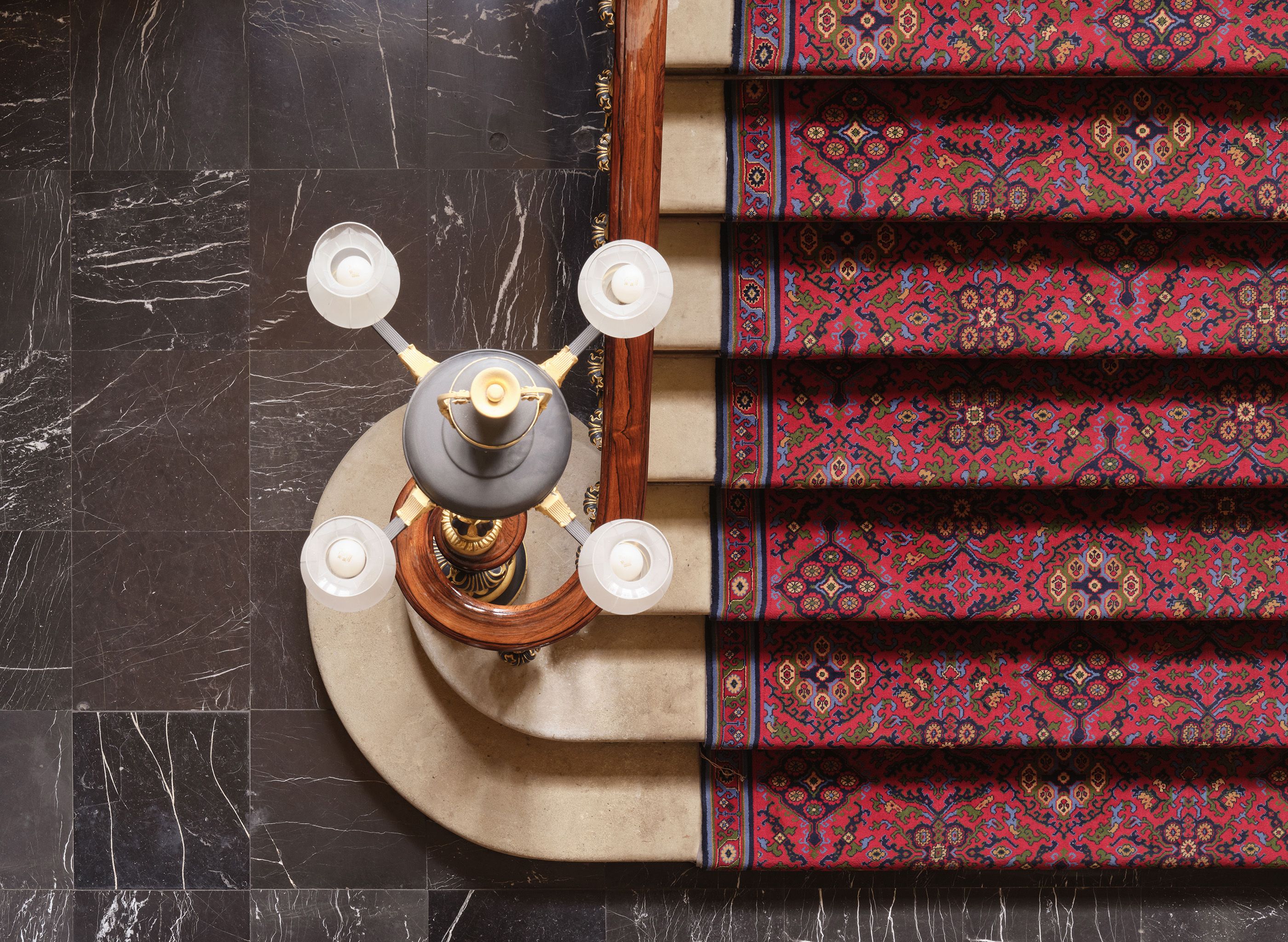 Birdseye view of staircase showing the top of a four arm light and red patterned carpet