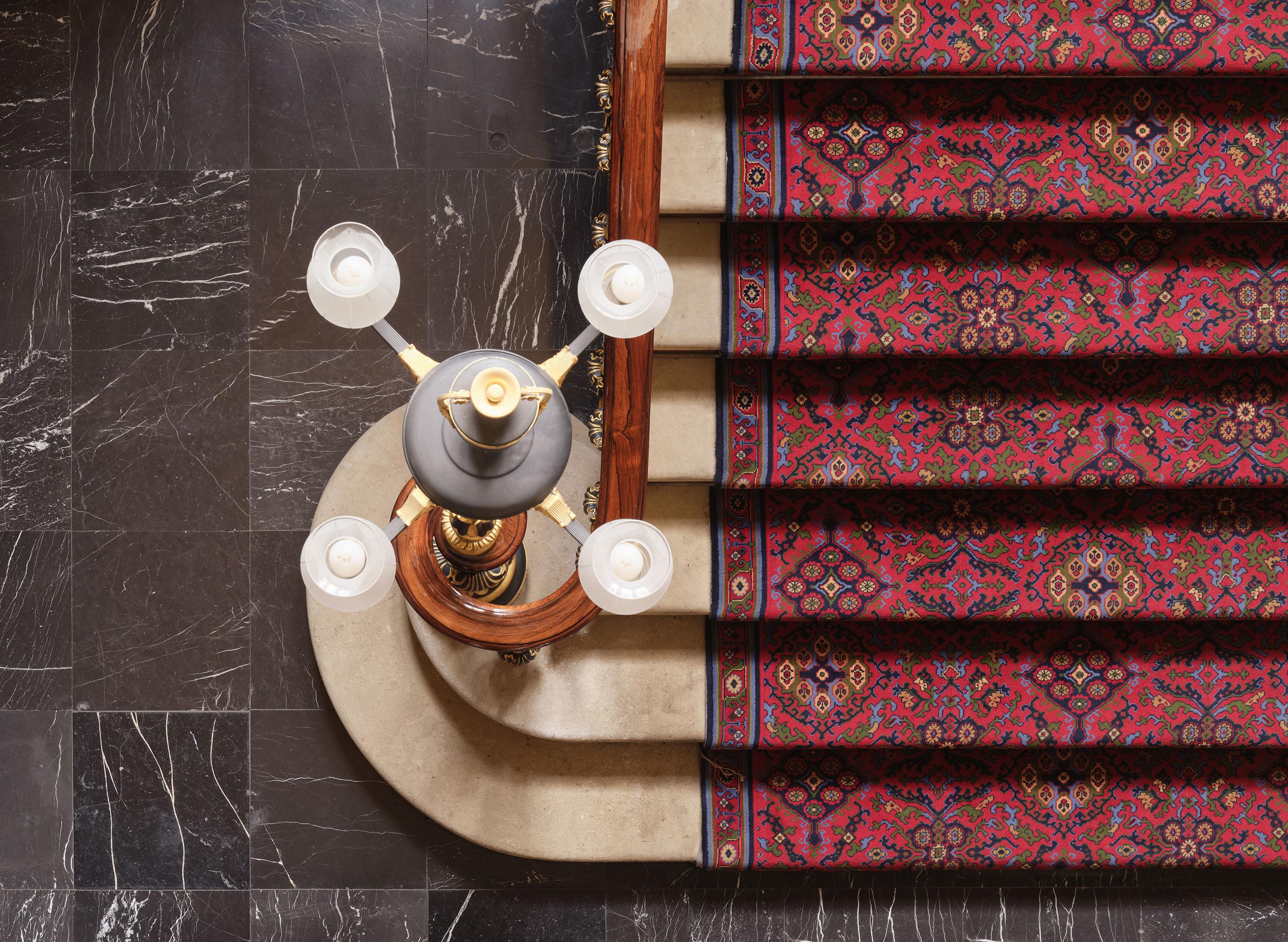 Birdseye view of staircase showing the top of a four arm light and red patterned carpet