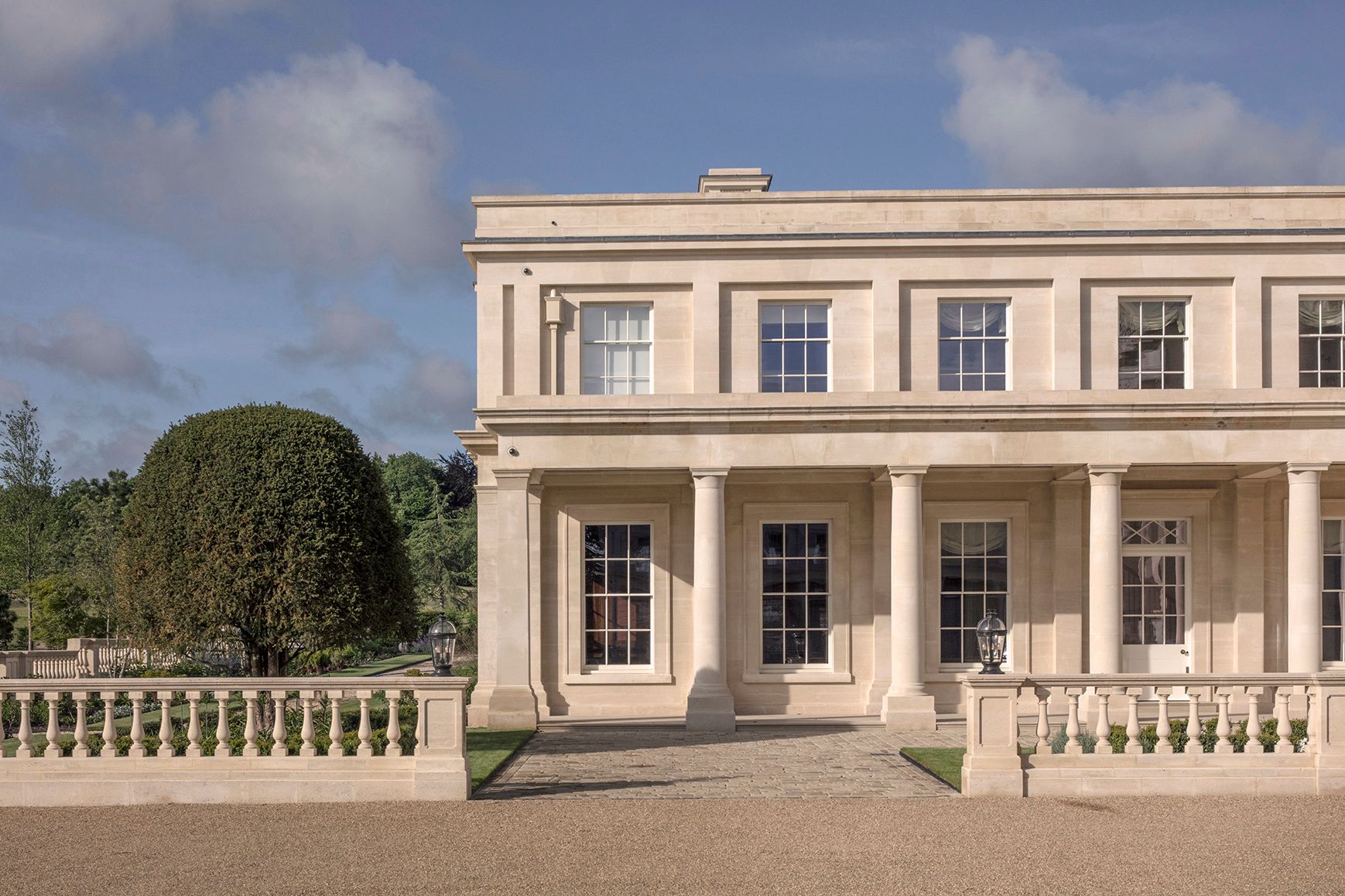 Exterior elevation of side wing, constructed in natural stone, with a metal sphere sculpture in the centre of formal gardens
