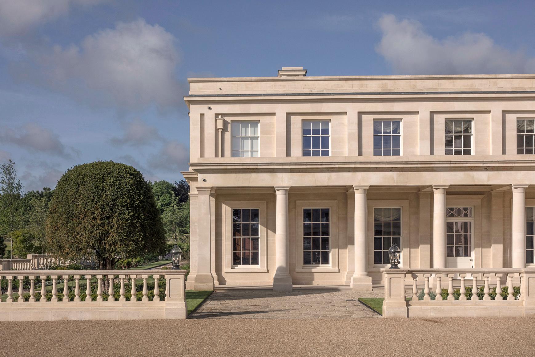 Exterior elevation of side wing, constructed in natural stone, with a metal sphere sculpture in the centre of formal gardens