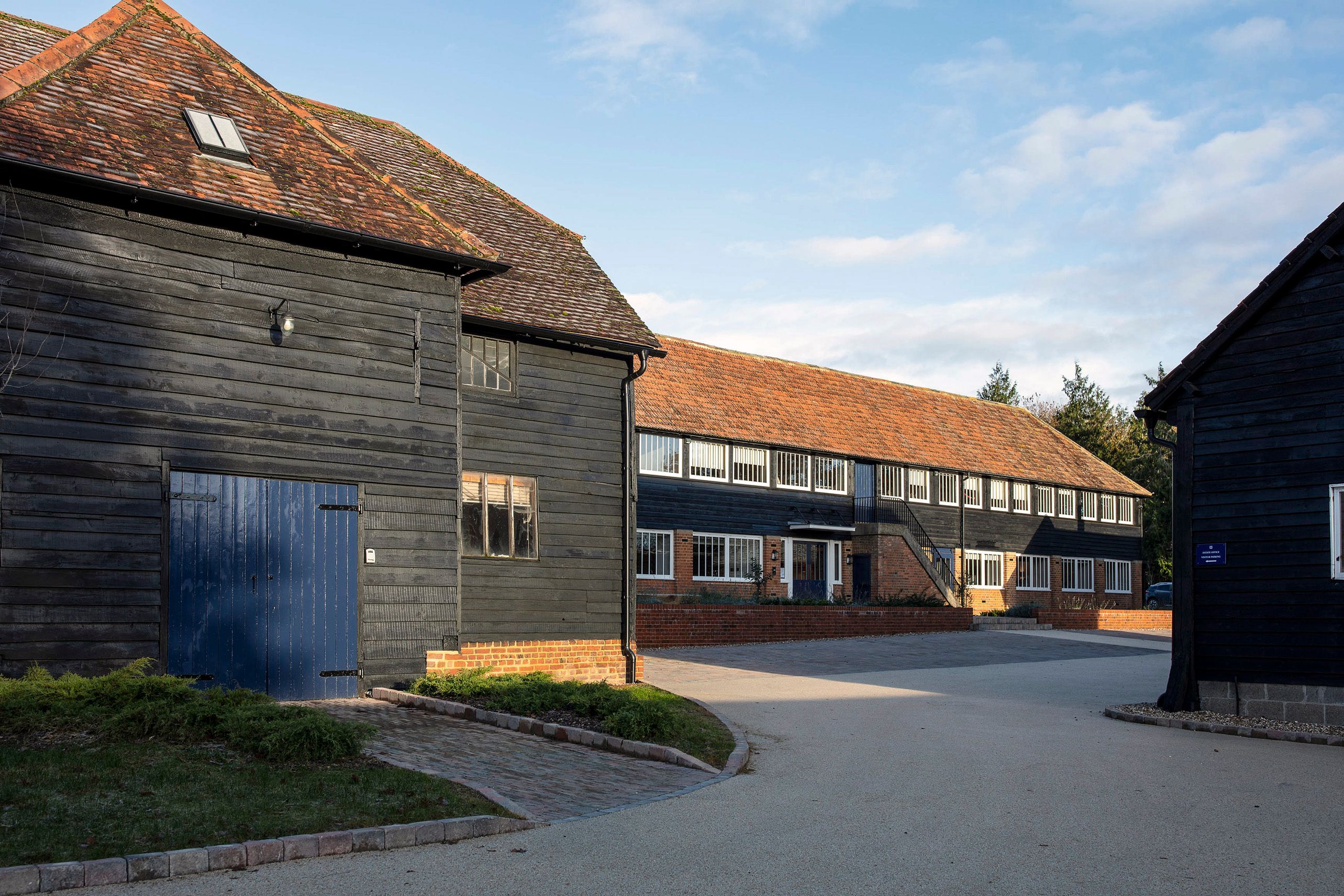 Front elevation and outbuildings all clad in matching black wood with navy blue painted doors