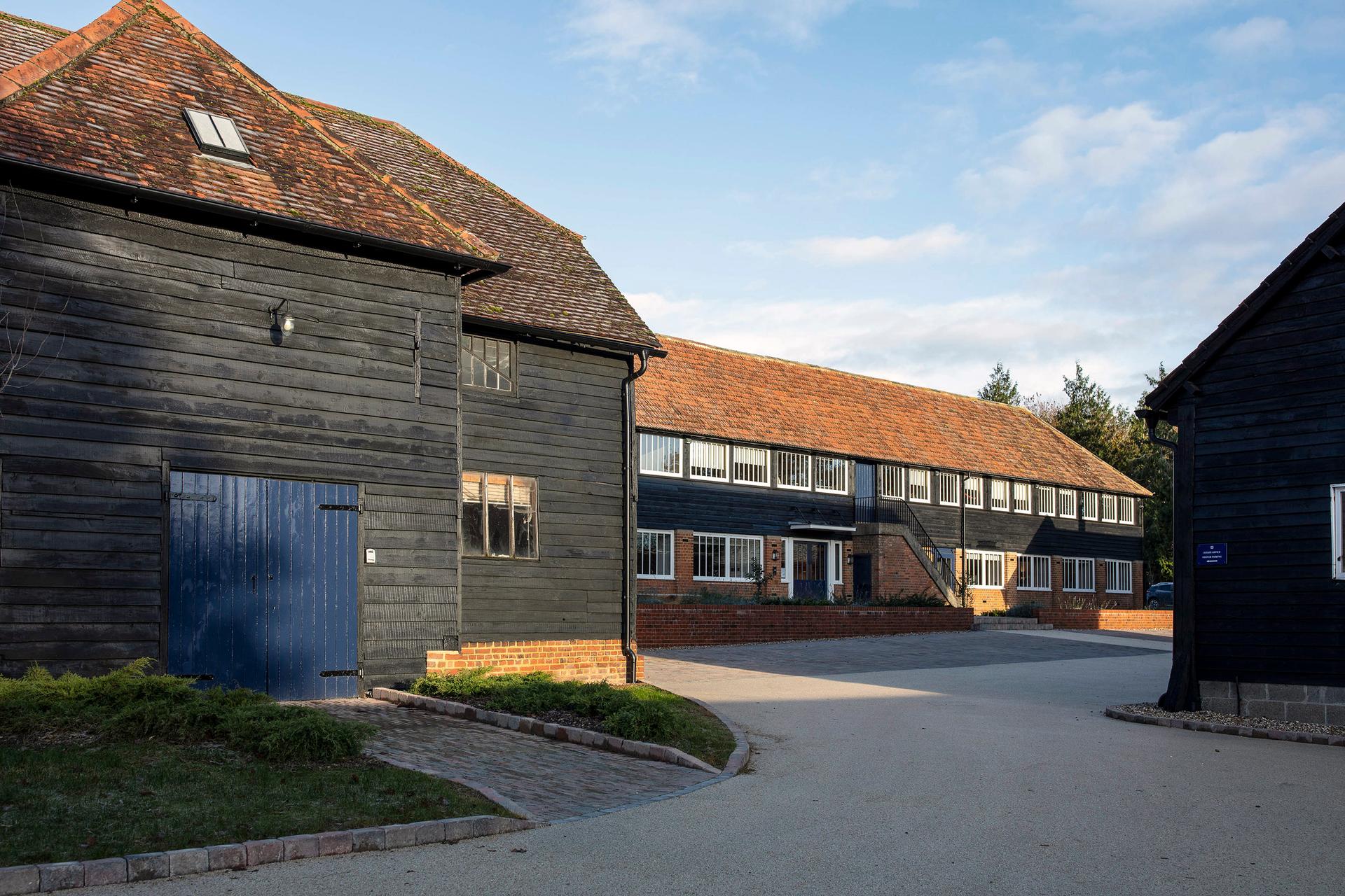 Front elevation and outbuildings all clad in matching black wood with navy blue painted doors